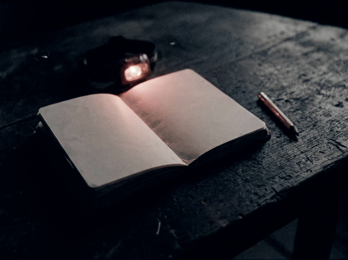 An open journal and a pencil under a red headlamp.