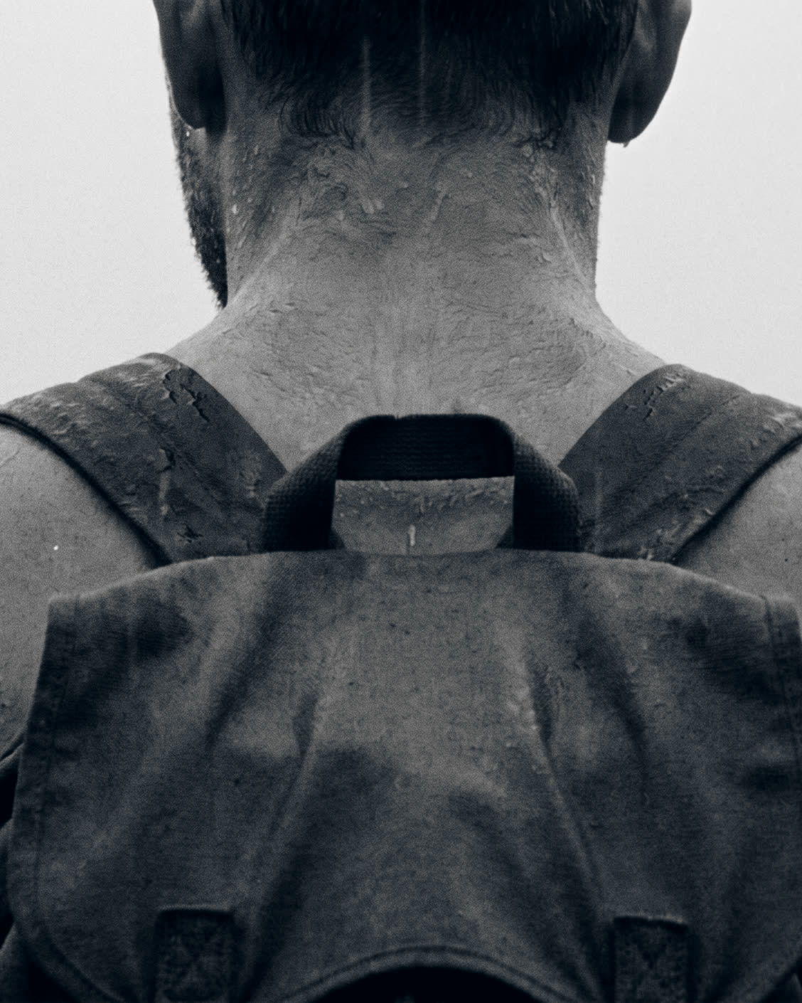 A soaked back under the weight of a rucksack, straps cutting in.